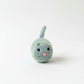 A small, crocheted toy cat with a pink nose and eyes sits on a plain white background.