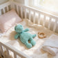 A cozy white crib with a plush green knotted dino lovey and a wooden teething ring on the bed.