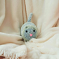 A crocheted cat toy with a pink nose sits on a soft, fluffy white blanket.