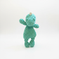 A small, green, Crocheted toy resembling a dinosaur is standing upright on a white background.