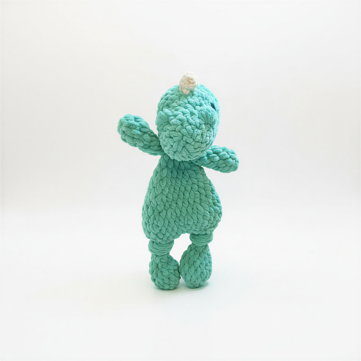 A small, green, Crocheted toy resembling a dinosaur is standing upright on a white background.